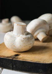 still life, champignon mushrooms on a cutting wooden board with black background
