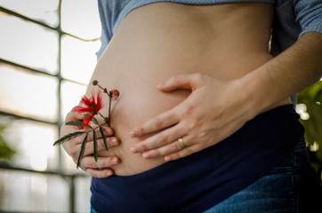 Panza de embarazada de perfil izquierdo con ambas manos y flor roja
