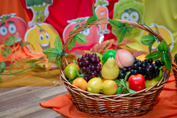 Cucumber, red pepper, carrot, potato, grape in the basket . Basket and artificial fruits on wooden table. Table-still life. The fruits are in the basket.
