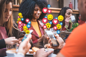 Social network emoticons that pops up over the smartphones of a young group of people sitting at a...
