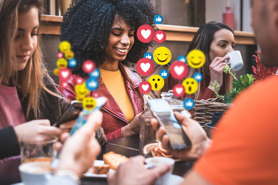Social network emoticons that pops up over the smartphones of a young group of people sitting at a coffee table having breakfast together. People using social media application concept.