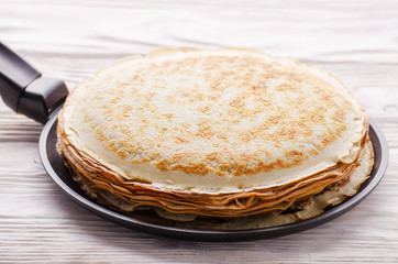 Stack of French crepes in frying pan on wooden kitchen table