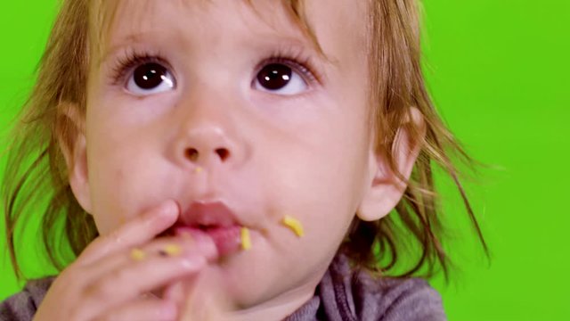 Happy  little toddler plays and eats with her hands, close-up, over green screen.