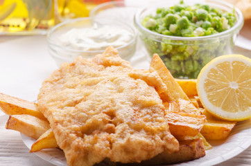 Traditional British street food fish and chips with tartar sauce and mushy peas on paper plate