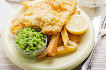 Traditional British street food fish and chips with tartar sauce and mushy peas on paper plate