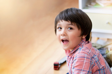 Portraot  Child sitting on wooden floor relaxing at home, Soft focus of Kid boy looking up with smiling face while playing alone in playroom. Positive children concept.