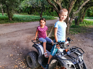 Fototapeta na wymiar Happy little children playing on road at the day time. They driving on quad bike in the park. Kids having fun on the nature. ATV