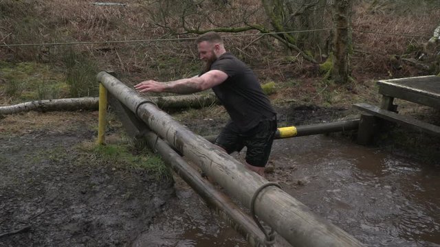 Bearded Man climbing out of cold, muddy water on a mud run / Obstacle / assault course - Super slow motion - Stock Video Clip Footage