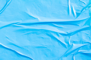 Blue crumpled creased paper placard poster glued on billboard background.