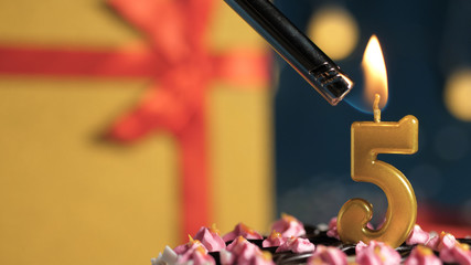 Birthday cake number 5 golden candles burning by lighter, background gift yellow box tied up with...