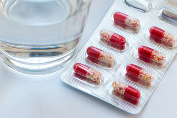 Capsules in blister with water in a clear glass cup on a grey surface. Medicine concept.