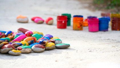 Many small pebbles covered with multicolored paint lie on surface