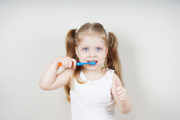 A little girl of European appearance brushes her teeth on a light background. The concept of...