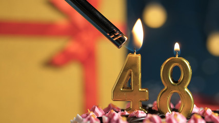 Birthday cake number 48 golden candles burning by lighter, background gift yellow box tied up with...