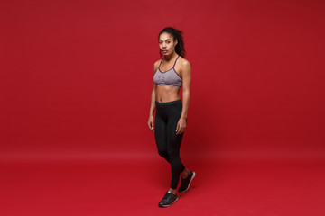 Beautiful young african american sports fitness woman in sportswear posing working out isolated on bright red background studio portrait. Sport exercises healthy lifestyle concept. Looking camera.