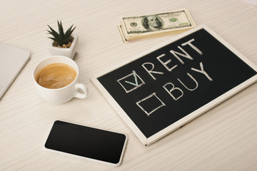 chalkboard with rent and buy lettering near cup of coffee, plant, smartphone with blank screen and money