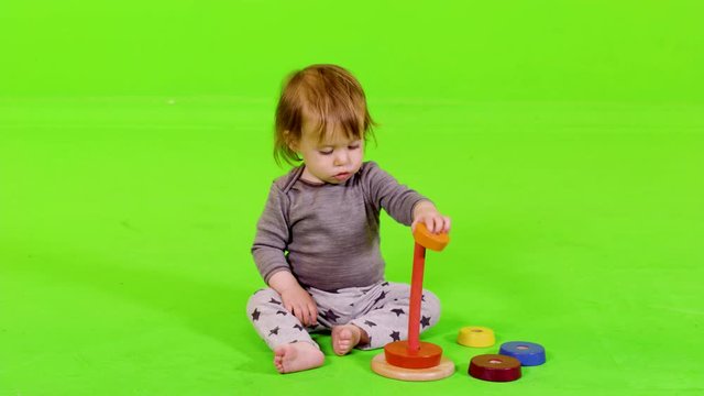 Cute toddler playing with rainbow stacker toy, clapping her hands after succeeding, over green screen.