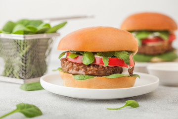 Healthy vegetarian meat free burgers on round ceramic plate with vegetables and spinach on light table background.