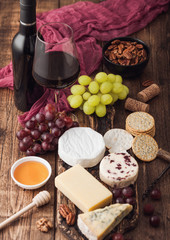 Glass and bottle of red wine with selection of various cheese on the board and grapes on wooden background. Blue Stilton, Red Leicester and Brie Cheese and bowl of nuts and crackers. Top view.