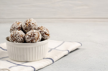 Energy balls of dates, nuts, oats, sprinkled with coconut powder closeup in a white plate on a white background background with copy space with place for your text. Healthy food. Raw dessert.