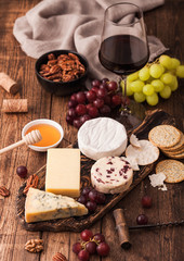 Glass of red wine with selection of various cheese on the board and grapes on wooden background. Blue Stilton, Red Leicester and Brie Cheese and bowl of nuts and crackers.