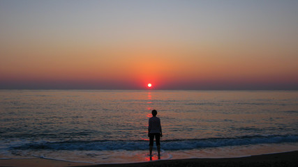 cloudless blue sky, sea, sun and silhouette of a man on the seashore during dawn
