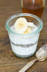 Organic yoghurt, sliced banana, chia seeds, served in a clean glass glass cup on a rustic wooden table. Healthy eating for weigh loss and health benefits.