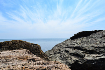 Fototapeta na wymiar blue sea, blue sky with white clouds and rocks in the foreground on a sunny summer day