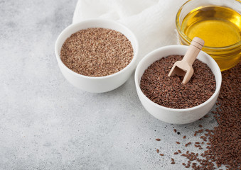 Bowl of raw natural organic linseed flax-seed with spoon and oil on light table background with linen cloth.