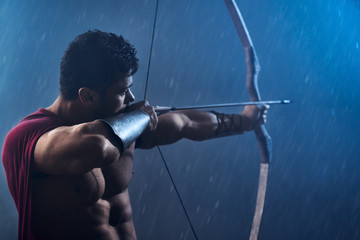 Muscular spartan in red cloak shooting from bow.