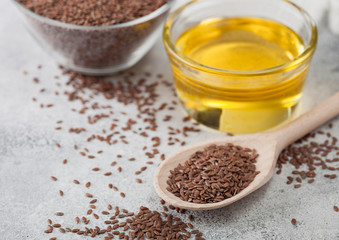 Bowl of raw natural organic linseed flax-seed with spoon and oil on light table background with linen cloth.