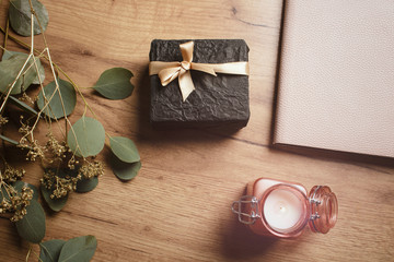 Beautiful gift on a wooden table with flowers, a notepad and a candle. Gift box. Holiday surprise. Lifestyle. View from above. 