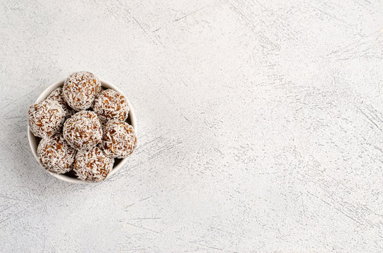 Energy balls of dates, nuts, oats, sprinkled with coconut powder closeup in a white plate on a white background background with copy space with place for text. Healthy food. Raw dessert.