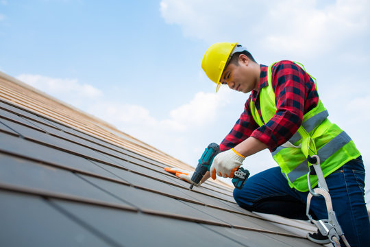 Construction Workers Fixing Roof Tiles, With Roofing Tools, Electric Drills Used On Roofs In Safety Kits For Safety.