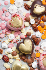 Assorted pink, orange, brown and green chocolate hearts with meringues, pecan nuts and chocolate drops on grey background