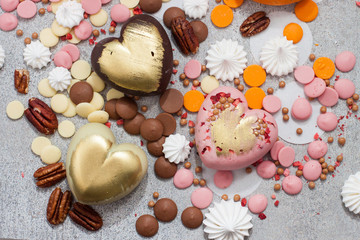 Assorted pink, orange, brown and green chocolate hearts with meringues, pecan nuts and chocolate drops on grey background