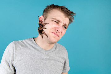 The man is disgusted by the fact that a large spider crawls across his face.