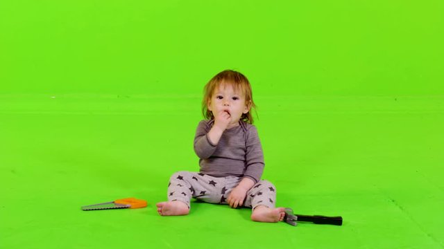Cute toddler playing with construction toys, putting her hands over her head, over green screen.