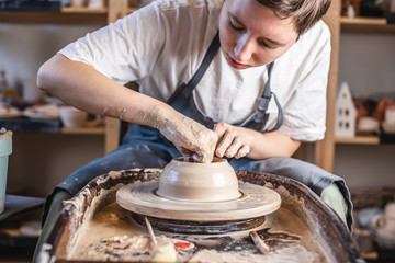 Potter working on a Potter's wheel making a vase. Young woman forming the clay with hands creating jug in a workshop.
