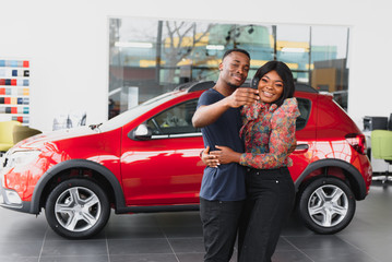 Fototapeta na wymiar Smiling African American couple hugging and smiling at camera at new car showroom
