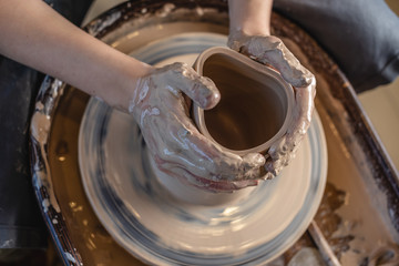 Potter working on a Potter's wheel making a vase. Woman forming the clay with hands creating jug in a workshop. Top view