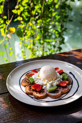 waffles with chocolate sauce, ice cream and strawberries and Kiwi on wood background