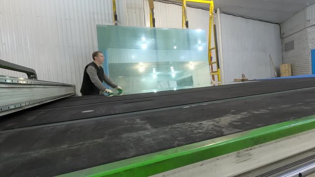 A worker drops a sheet of glass from the counter and pushes it across the table.