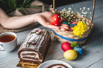 Festive Easter lunch with colorful bright eggs in a basket and an cake on a wooden table. Traditional spring holiday.