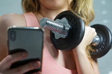 young caucasian woman in a coral top is doing a selfie while holding a dumbbell, closeup