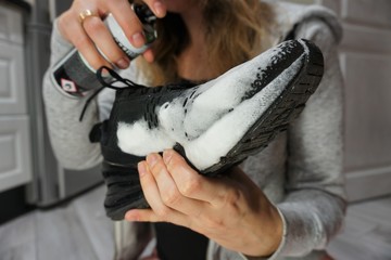 A woman sits on the floor and cleans sports shoes with a foam detergent, selective Focus, closeup.