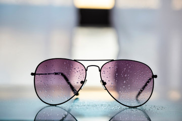 Primer plano de gafas de sol con gotas de lluvia en los cristales, reflejos y fondo desenfocado....