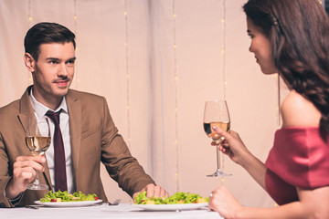 happy, elegant man and woman sitting at served table and holding glassed of white wine