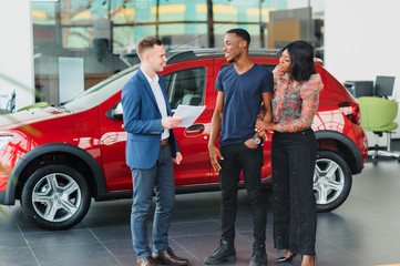 Smiling African American couple hugging and smiling at camera at new car showroom