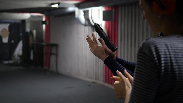 Rear view of a girl aiming at a target in a shooting gallery, holding a gun in her hands